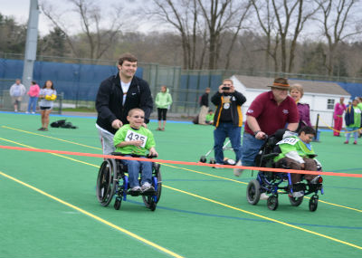Volunteers pushing children in wheelchair during Special Olympics.
