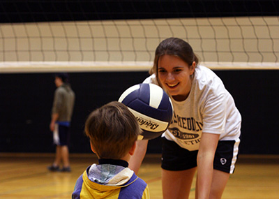 A female student teaching volleyball to a child.