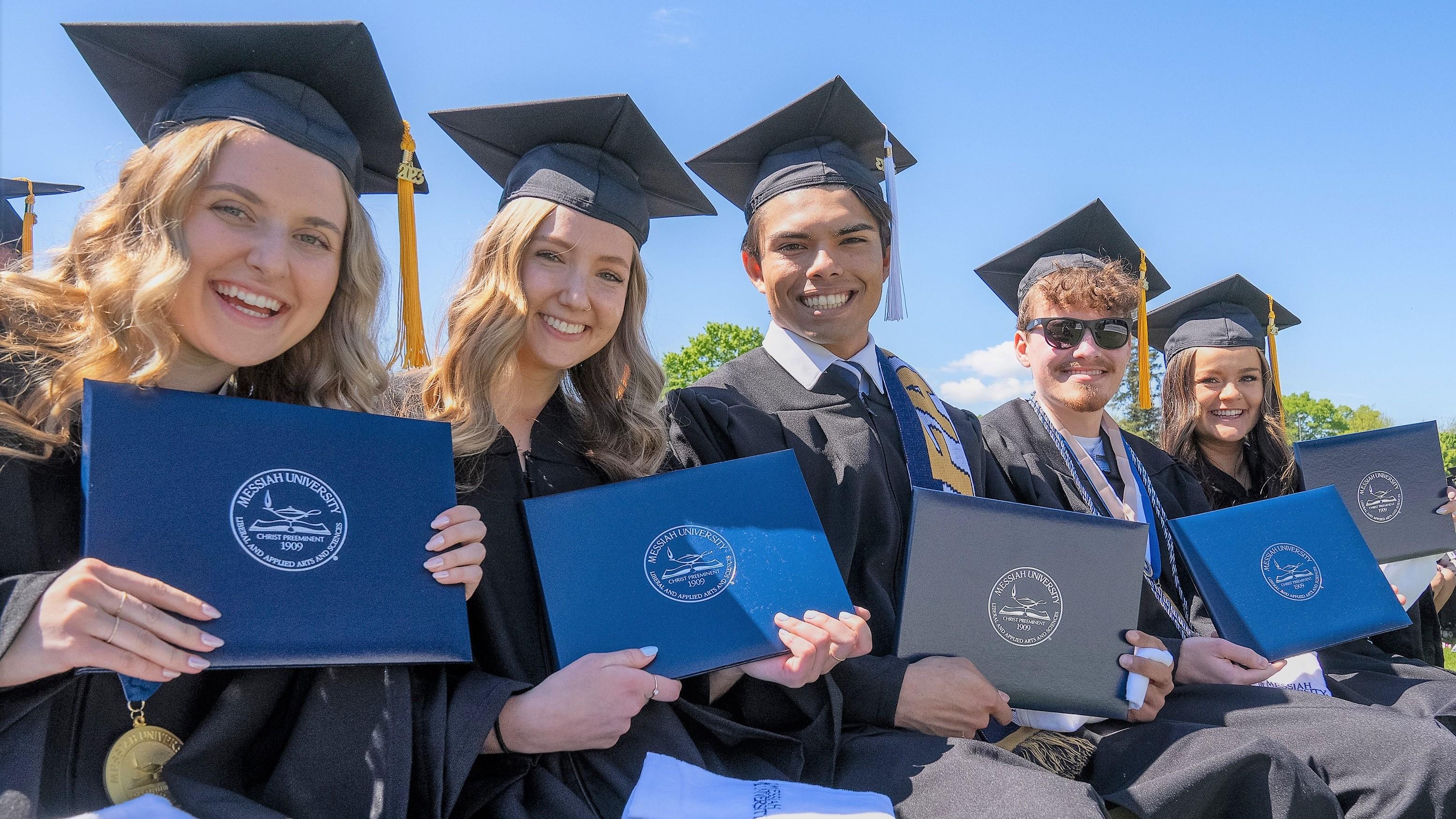 multiple UG students in commencement attire showing off their diplomas