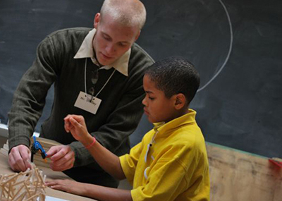 A college student teaching a young child how to make three dimensional sculptures.