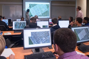 Students sit behind laptops that display images of historic maps.
