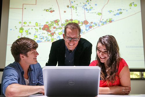 A professor and two students working together in front of an image of a map on the projector.