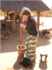 Student making peanut butter by using a large stick and a vessel on the ground