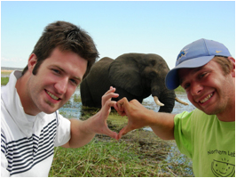 Two students making a "hand heart" near an elephant