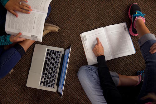 Students studying on the floor with their books and laptop on the floor.