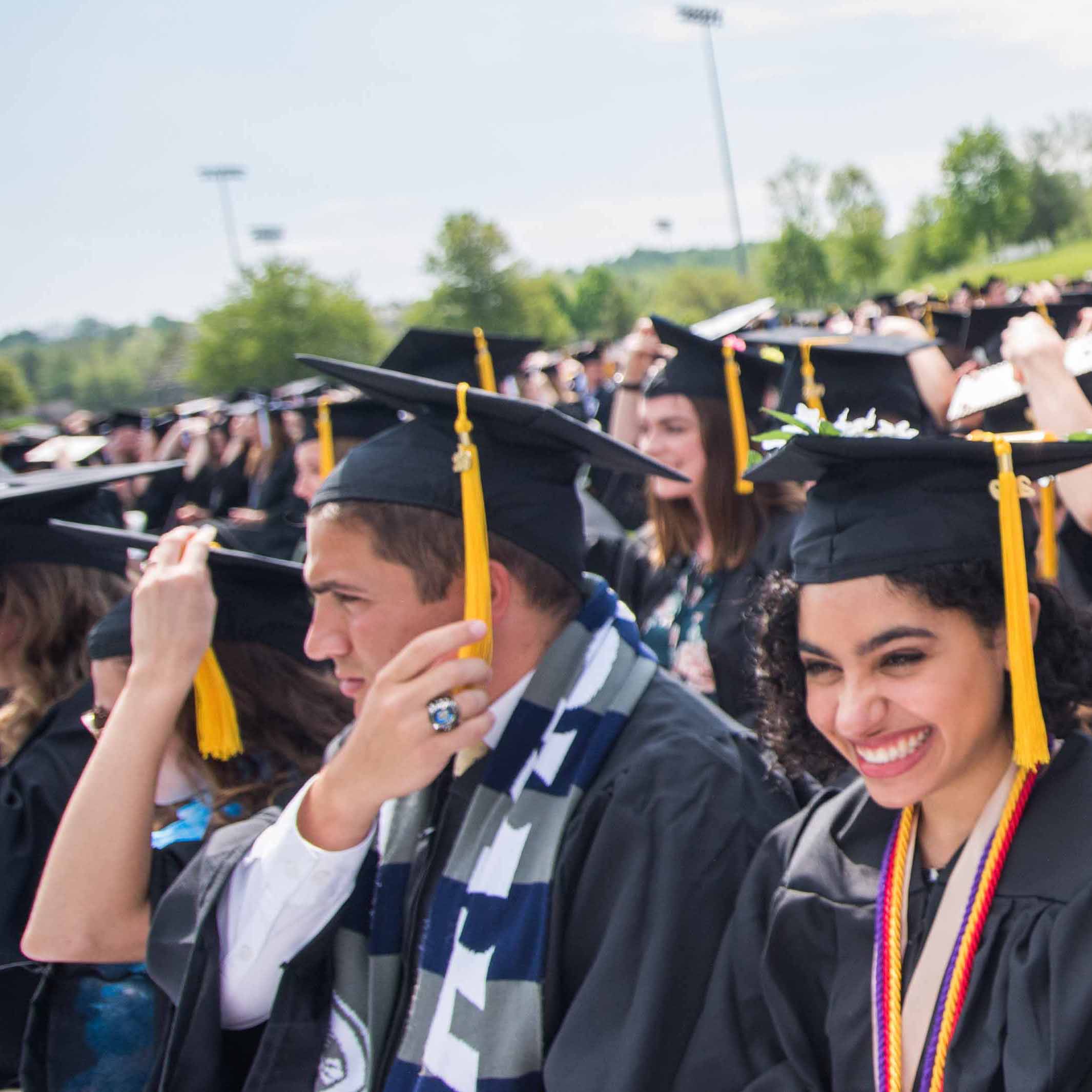 Male and female student at Commencement moving their cap tassels from right to left