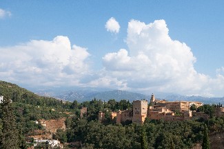 A scenic view of Spain with trees, rooftops and white clouds in the sky above the city.