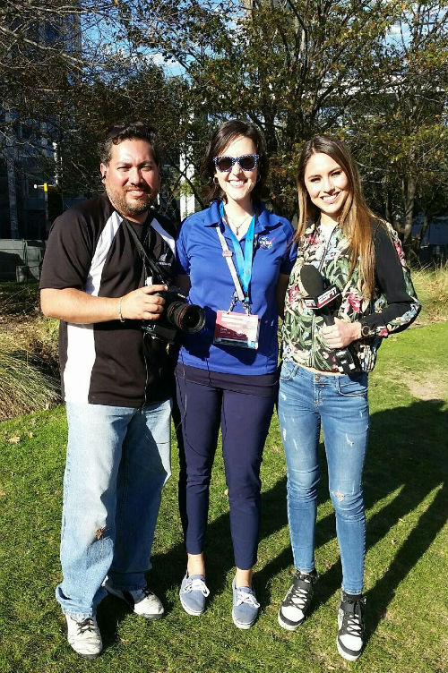 Two women and one man stand together outside smiling for the camera.