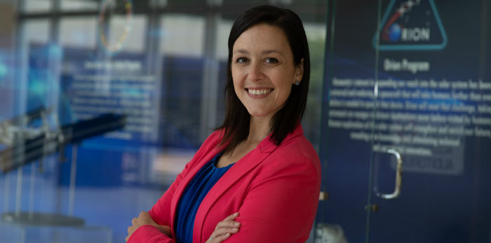 A woman stands in front of glass doors smiling wearing business clothing.