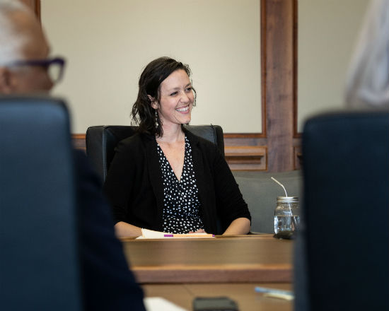 A woman sits at a table during a meeting smiling and looking to the side.
