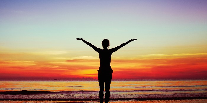 The silhouette of a person standing in front of a beach sunset.