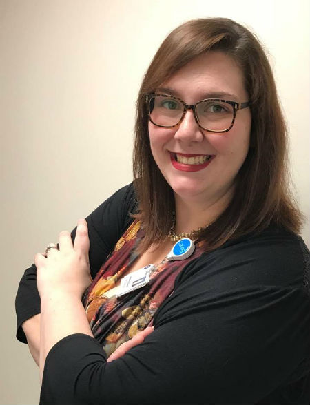 A woman wearing glasses stands smiling for the camera with her arms crossed.