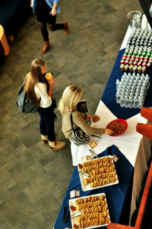 Two women stand at a table full of refreshments picking up food.