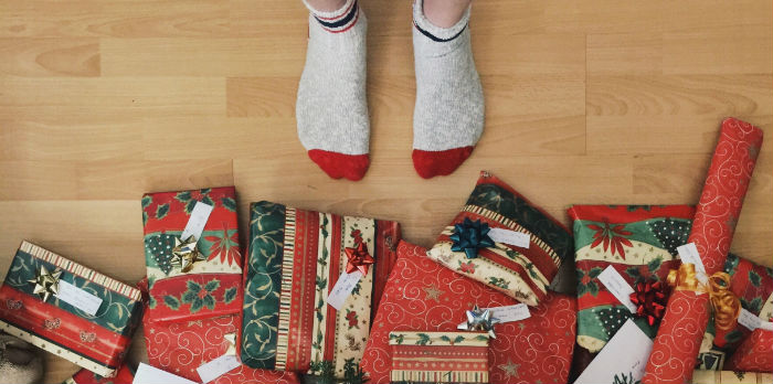 Feet with socks on stand in front of a pile of Christmas gifts.