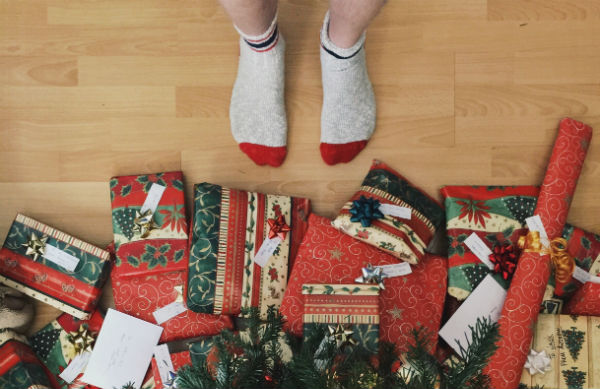 Feet with socks on stand in front of a pile of Christmas gifts.
