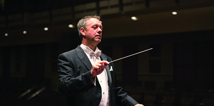 A conductor wears a suit and is conducting a musical ensemble