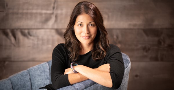 Headshot of a female author in a chair in front of a wooden wall.