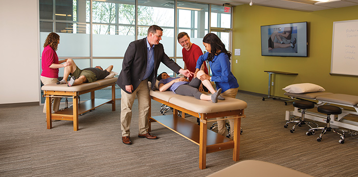 Two people lay on tables as men and women stand over them.