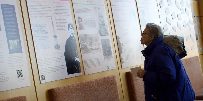An older woman stands looking at plaques on the wall reading about history.