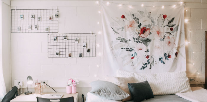 A feminine dorm shows a bed, desk, decorations and string lights on the wall.