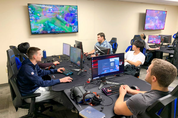 Male students sit at desktop computers playing competitive video games.