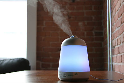 An essential oil diffuser sits on a wooden table in front of a brick wall.