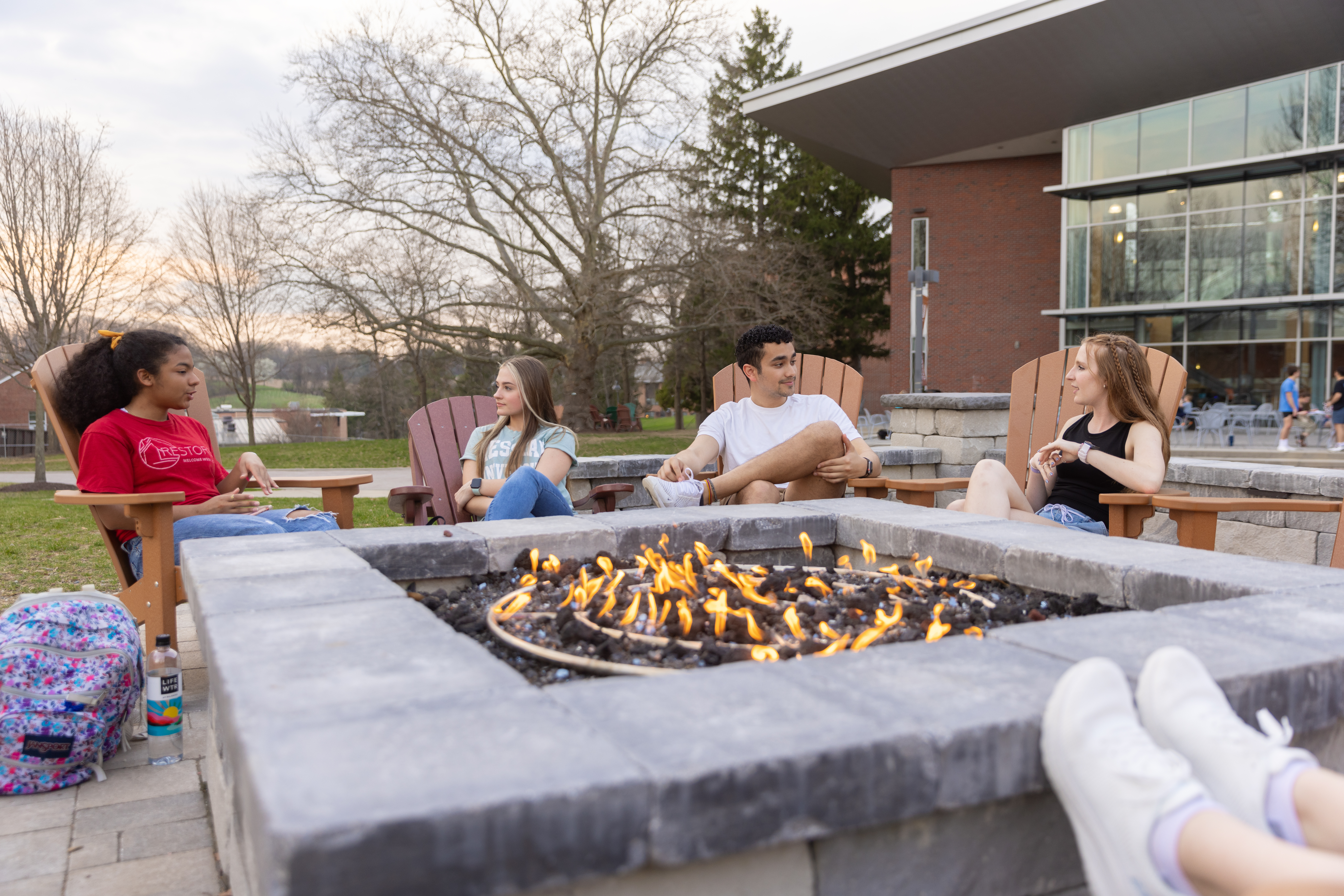 Students gathered and talking around outdoor firepit.