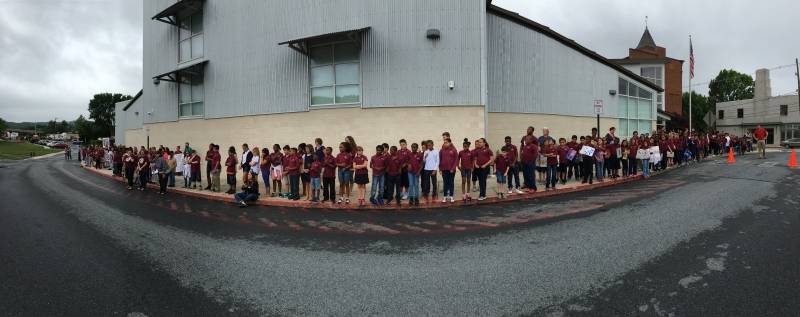 Many Elementary aged children standing in front of a school building. 