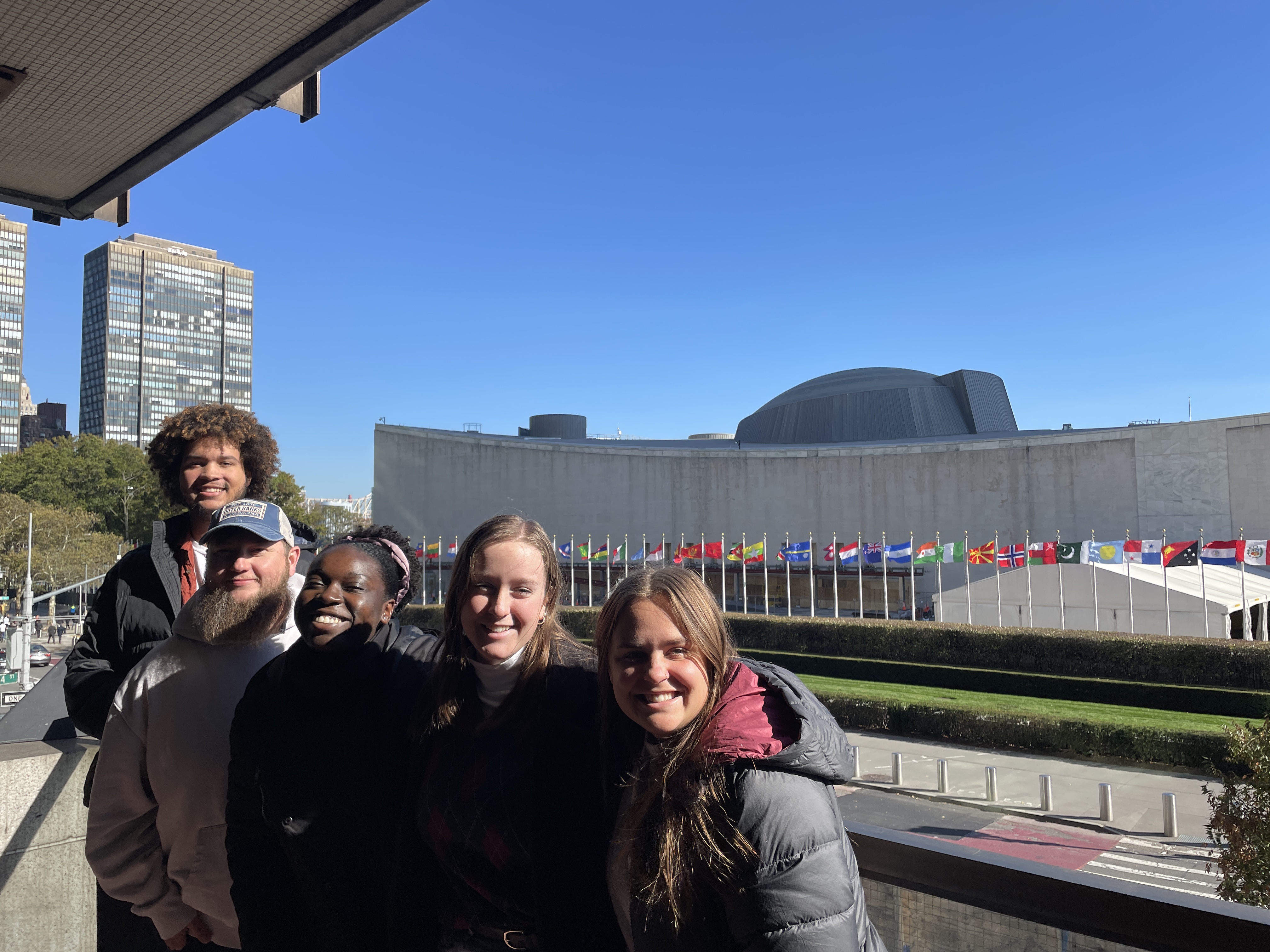 Group of students on a balcony overlooking the UN entrance with all participating countries' flags.