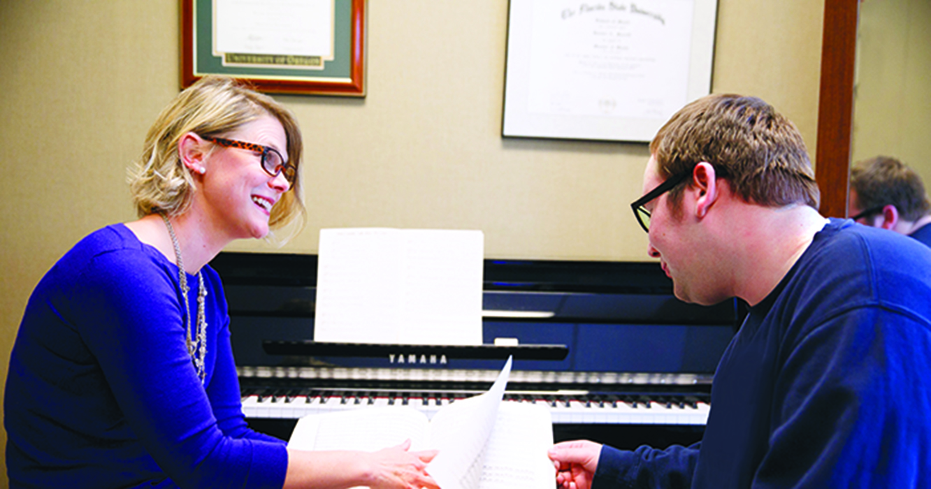 Two individuals sit at a piano, looking at sheet music.