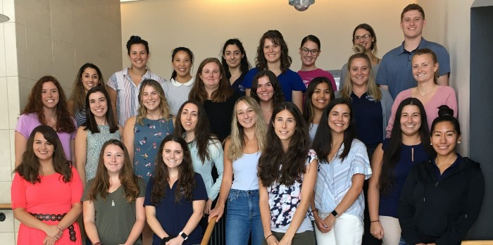 A large group of mostly women stand together for a group photo smiling.