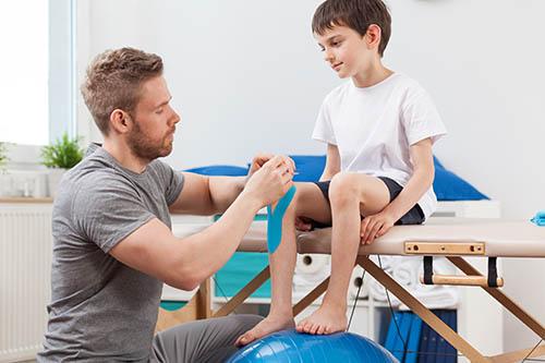 Physical therapist taping a child's knee.