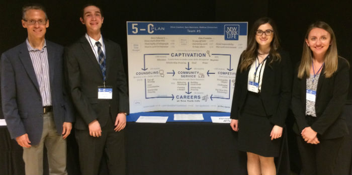 Two males and two females stand in front of a poster wearing dress clothing.