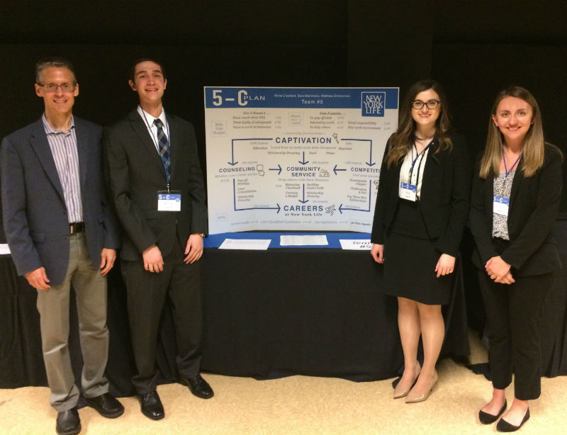 students in dress clothes stand next to their poster at the marketing competition
