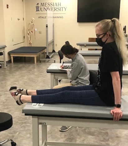A female dancer sits on a doctor's table while an athletic training student helps her.