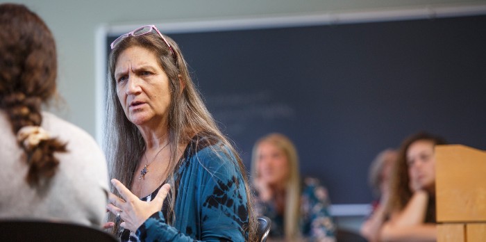 A woman sits in a classroom talking to a student.