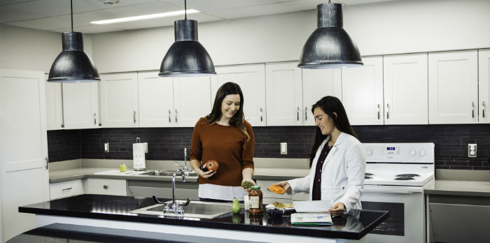 Two females stand in a neat kitchen preparing food for a lab.