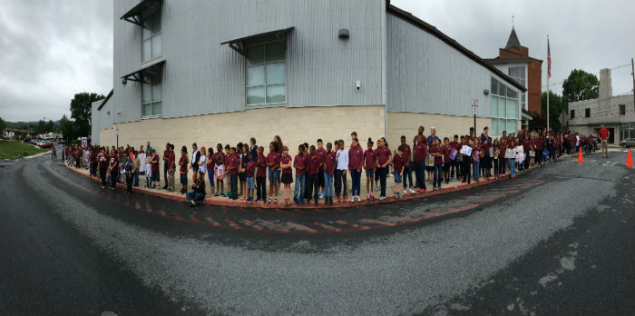 Many elementary aged children in uniforms, standing in front of a school building.