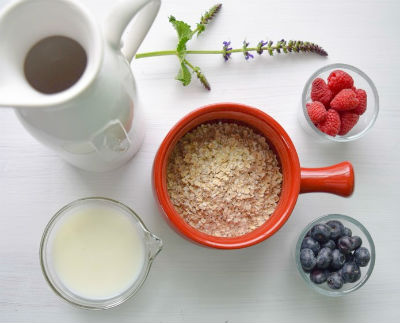 Oatmeal, berries, milk and coffee sit on a white table
