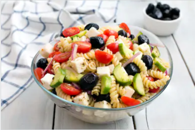 A bowl of pasta salad with tomatoes, noodles and other vegetables on a table.