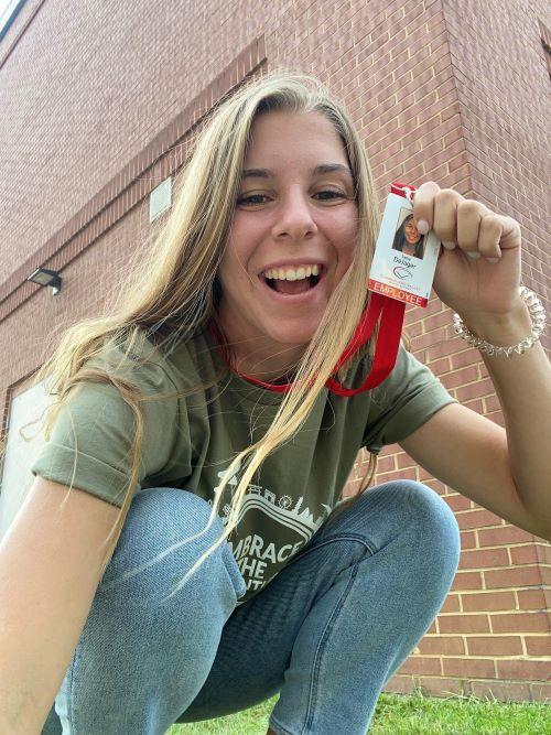 Sadie DeJager is crouched in front of school building lifting up her lanyard with ID.