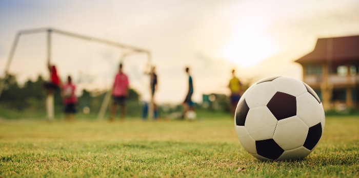 A soccer ball in the forefront of young people playing soccer.
