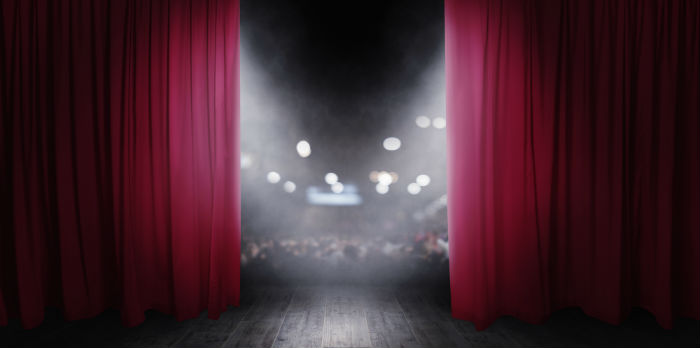 Red curtains on a stage open up to show lights out in the audience.