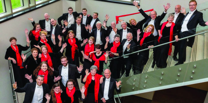 Men in tuxedos and women in red dresses stand posed on a flight of stairs.