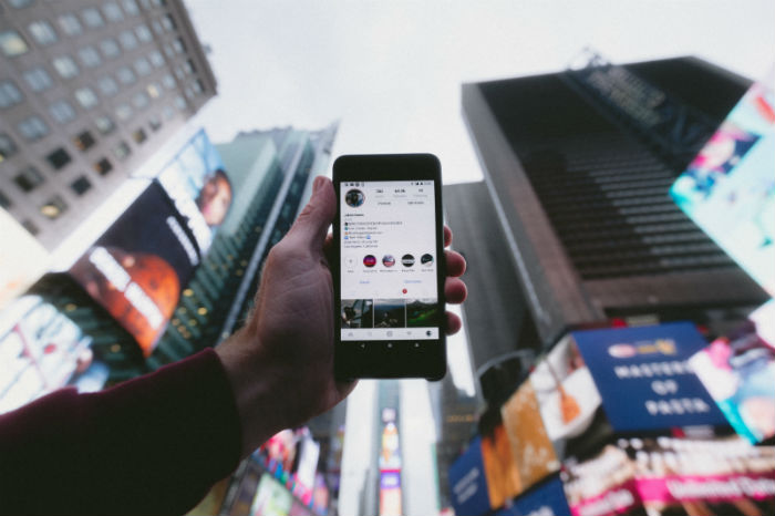 A hand holds an iPhone toward the sky while city skyscrapers are shown in the background.