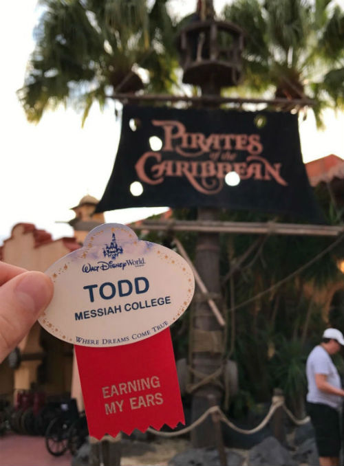 A nametag saying "Todd" is held in front of the Pirates of the Caribbean ride in Disney World.