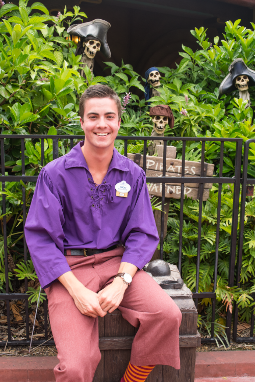 A male student sits in a pirate costume in front of green bushes.