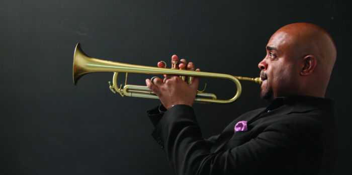 A man in a black suit plays a trumpet.