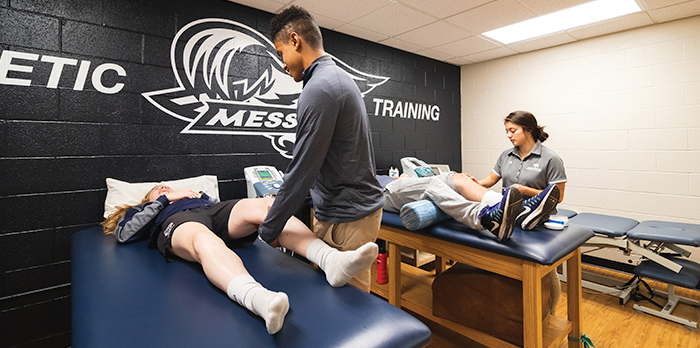 Two athletic training students attend to patients laying on beds.
