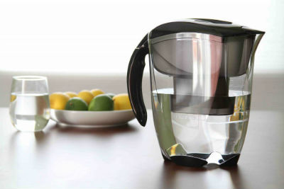 A water filtering pitcher sits on a counter in front of a bowl of lemons and limes.